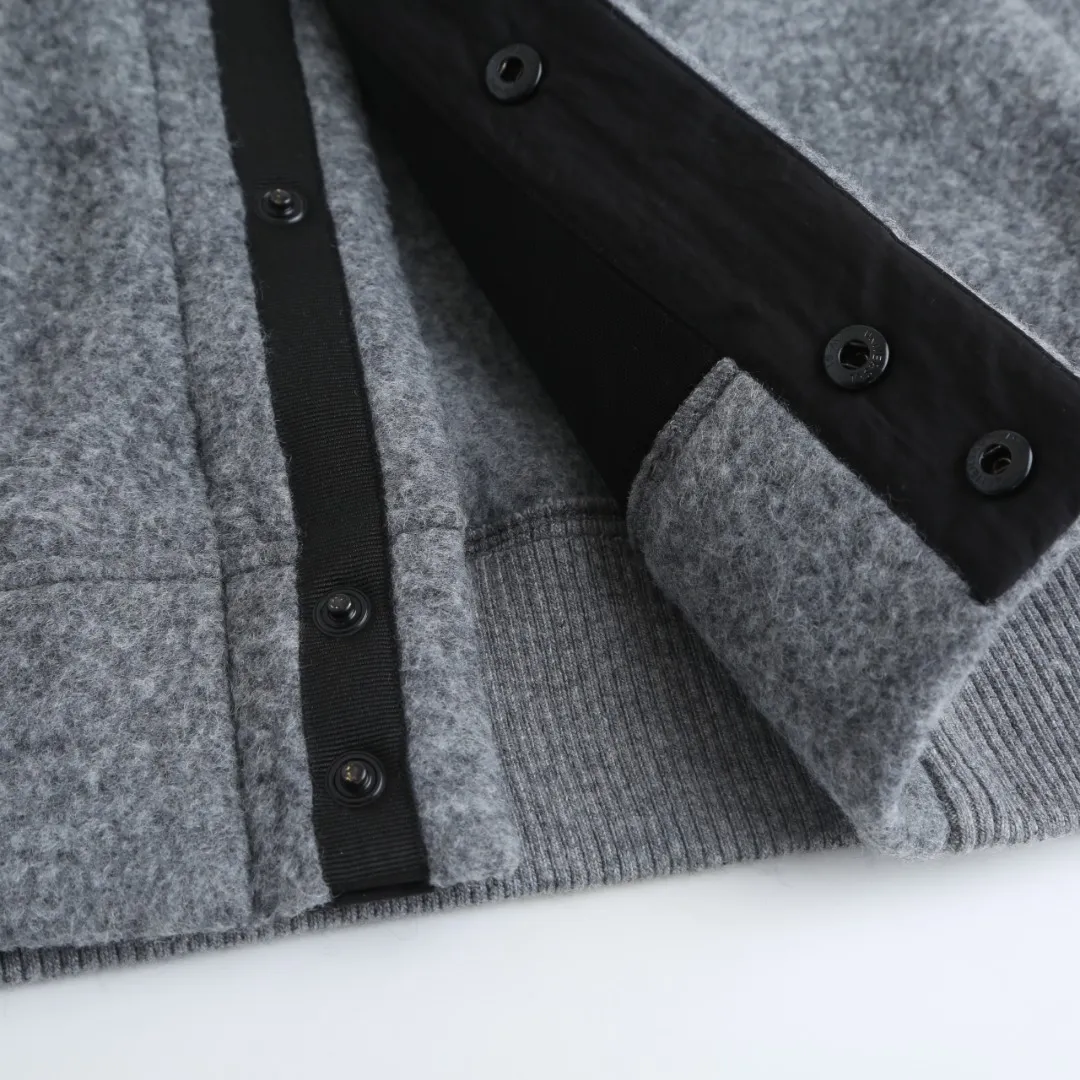 P760 Canada Goose Fleece Badge Button Jacket Fabric selection: Wool blend fabric: The main fabric of this jacket is light gray wool blend fabric to improve the fabric's wear resistance, wrinkle resistance and warmth. Wool provides good warmth and a natural feel, while blended fibers enhance the fabric's practicality and durability.  RIBBED KNIT: The collar, cuffs and hem are ribbed knitted for added stretch and fit.  Production process: The cutting process needs to ensure that the texture and color of the fabric are evenly distributed, especially for this light gray tone, to avoid color differences. The stretchability of wool-blend fabrics needs to be taken into consideration when cutting pieces to ensure dimensional stability of the finished garment.      • Use a sewing needle and thread suitable for wool-blend fabrics to avoid damage to the fabric during sewing. The sewing stitches are even and firm to prevent thread stripping.      • The temperature needs to be controlled during ironing to avoid high temperature damage to the fabric while keeping the fabric smooth and crisp.  Main body splicing: • The front and back body parts, sleeves and other main parts are spliced ​​with flat seams to ensure a smooth silhouette. •Align the fabric texture at the splicing points to keep the appearance neat.     Details such as pockets and cuffs are designed with inset pockets to increase practicality and aesthetics.     The splicing areas are reinforced to improve durability.  Armband: The white round armband on the left arm is an important part of the brand identity and is finely sewn to ensure it is strong and flat.  Dark gray and light gray Size: S M L XL